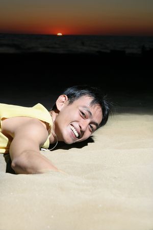 man putting hand in the beach sand, sunset at distanceの写真素材
