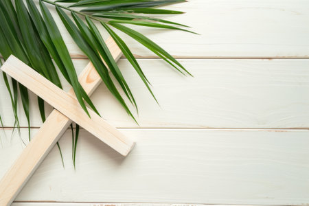 A cross and a palm leaf on a white wooden background. Palm Sunday, wooden christian cross with palm leaf on textured light background.の素材