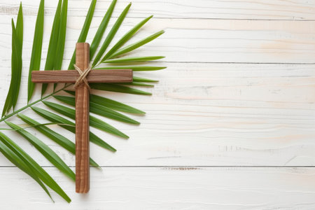 A cross and a palm leaf on a white wooden background. Palm Sunday, wooden christian cross with palm leaf on textured light background.の素材