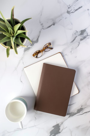 A beautifully arranged composition features a marble table adorned with a notebook, glasses, and a vibrant plant, creating a tranquil and artistic scene. Blank mockup, copy-space.の素材
