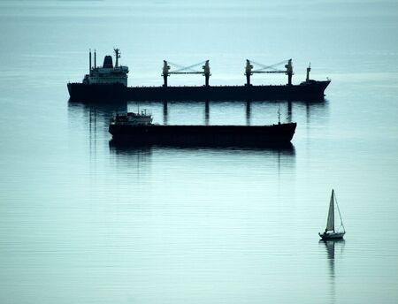 Two freight boats on the sea and a small sailing boatの写真素材