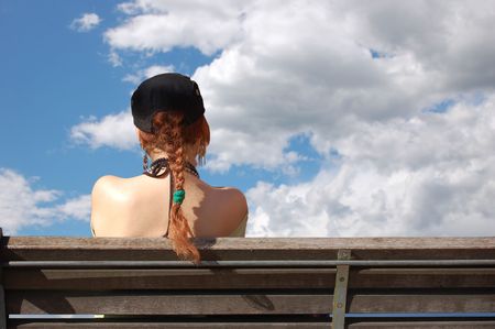 Girl sitting on a bench and watching the clouds in the backgroundの写真素材