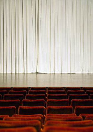 Theater stage with white curtain in the background and red seats in the frontの写真素材