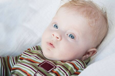 Little boy lying in white sheets, distracted by the camera