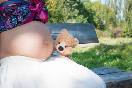 Pregnant woman holding teddy bear next to her bellyの写真素材