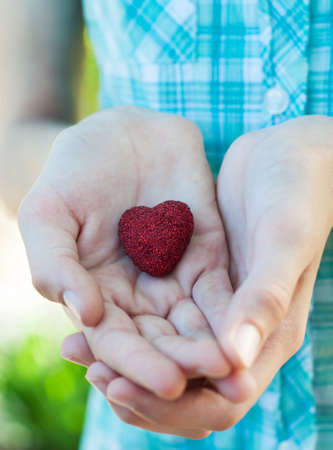 Hands holding a red heart on a nature backgroundの写真素材