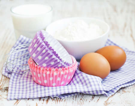 Cupcake cases and ingredients for muffins on a wooden background