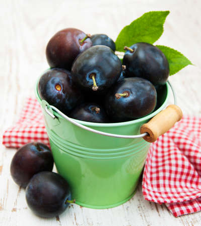 Fresh purple plums in a bucket  on the wooden backgroundの写真素材