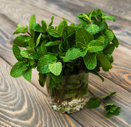 Bunch of fresh mint in a glass of water on wooden background