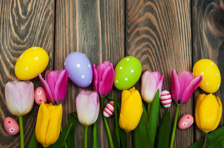 Colorful tulips and easter eggs - border on a old wooden background
