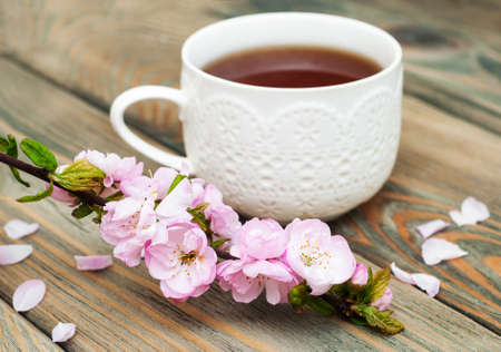 Cup of tea and pink sakura blossom on a old wooden backgroundの写真素材