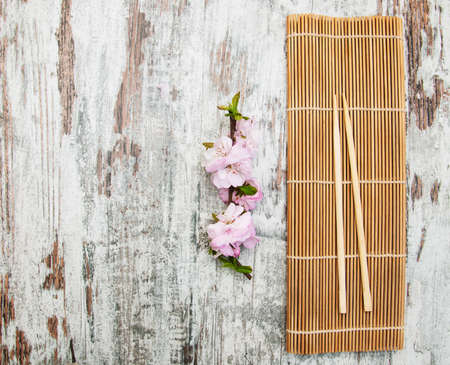 Pink sakura branch and sticks over  bamboo mat on a old wooden tableの写真素材