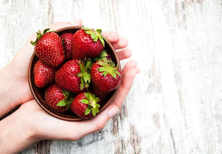 strawberry in bowl with hands against wooden backgroundの写真素材