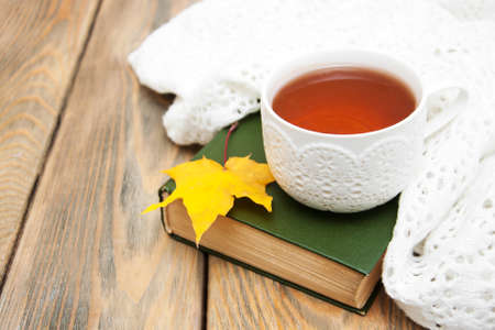 Cup of tea with scarf and autumn leaf on a old bookの写真素材