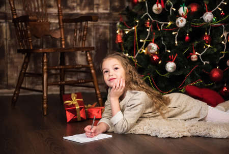 girl writes letter to santa near christmas treeの写真素材