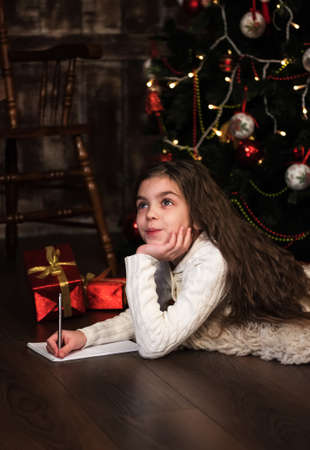 girl writes letter to santa near christmas treeの写真素材