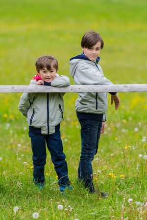 Two boys leaning over a rustic wooden fenceの写真素材
