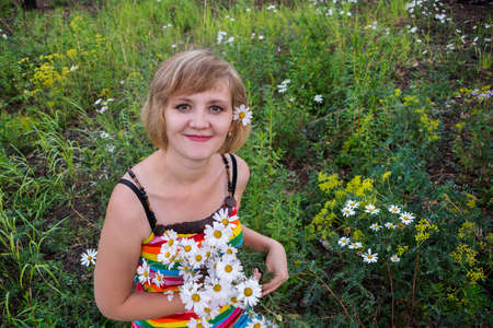 Portrait of beautiful young woman with white chamomiles in hair and in the hands of. The girl looks to the sideの写真素材