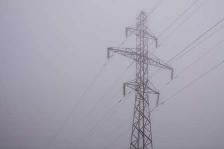 electric pylon and power line in morning fog. Dim world in obscure.の写真素材