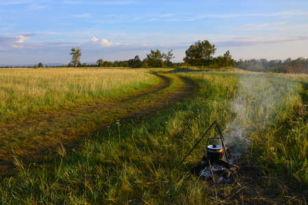 a kettle hangs over the fire, in which water for coffee is heated. A summer tour in nature. Landscape with grass field and skyの写真素材