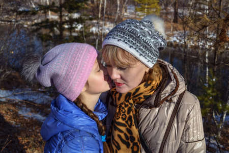 Daughter whispering something to her mother in the autumn forest. Family, child, relationships and happiness concept - smiling mother and daughter whispering gossip.の写真素材