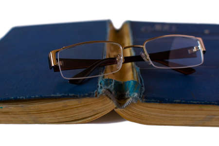 Old book with reading glasses resting on white table