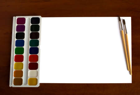 Set of watercolor paints, brushes for painting and blank white paper sheet on wooden background.