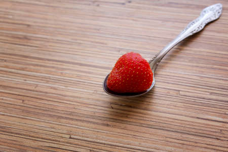 A single strawberry in small spoonl on wooden table backgroundの写真素材