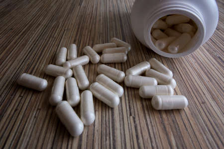 Pile of scattered capsules on a wooden background. white capsule pharmacy bottle pill drug conceptの写真素材