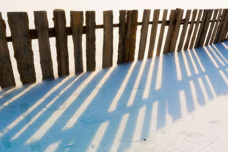 A wooden fence and its shadow on snow.の写真素材