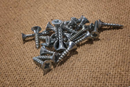 Pile of screws on wooden background. Tapping screws made of steel, iron screw, screws as a...