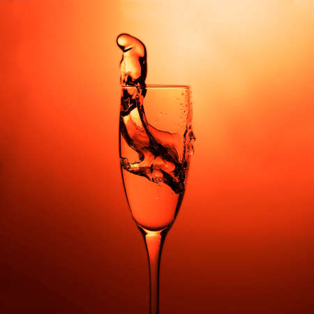 Elegant cocktail glass with splash of drink. Close-up view of the splash drink on a colorful red backgroundの写真素材