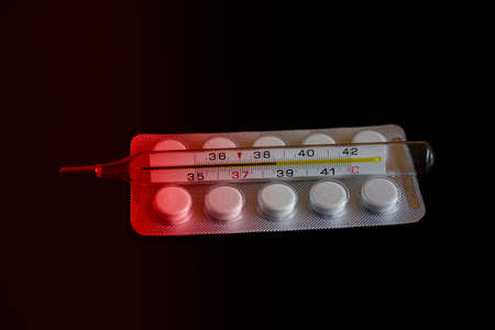 Various medications and mercury thermometer lie on a dark background. The red gradient indicates a high temperature hazardの写真素材
