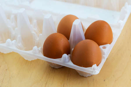 Four eggs in a container above a wooden tableの写真素材