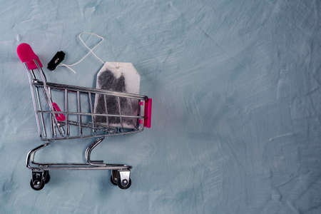 Tea bags in toy shopping trolley on gray background. Conceptual photo. Side view with some copy space.の写真素材