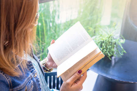 woman reading a book sitting on chair near the window