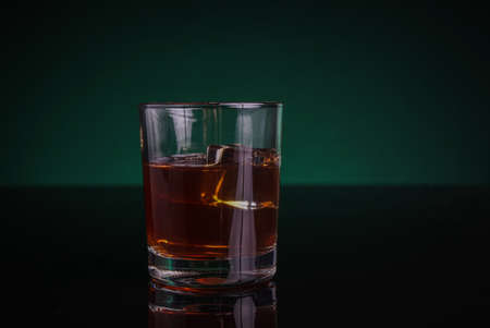 A glass of whisky or rum, with green backlightの写真素材