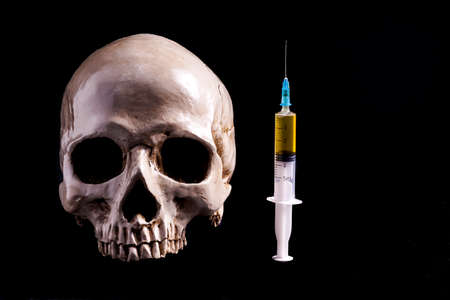 Skull and syringe of yellowish liquid . The syringe is filled with medicine , poison or drugs. Isolated on blackの写真素材