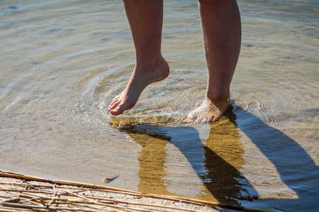 young lady dips her feet in the cool lake water on a sunny dayの写真素材