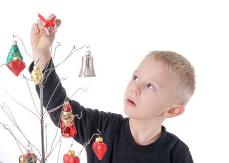 Cute little Boy decorates metal Christmas tree with beautiful glass Christmas ornaments, isolated on whiteの写真素材