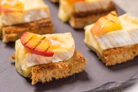 canapes, Appetizer with grilled brie and nectarine plated on a slate dish
