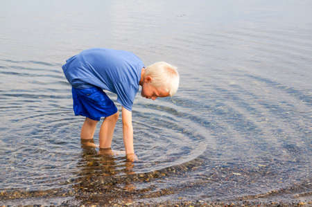 A little boy goes with his feet in the water on the beach and looking for clams and crabsの写真素材