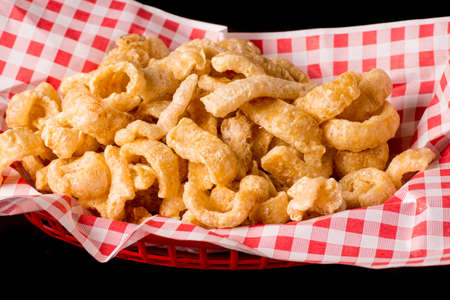 Delicious crispy pork rinds. A crisp salty snack on black glossy background