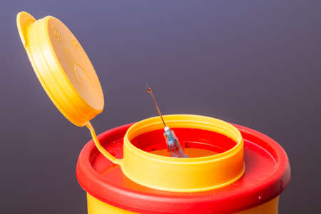 Yellow medical needle disposal waste container, syringe needle with red drop on the tip. Isolated