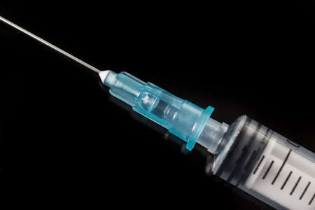 Empty disposable syringe. Closeup of the tip and needle isolated on black backgroundの写真素材