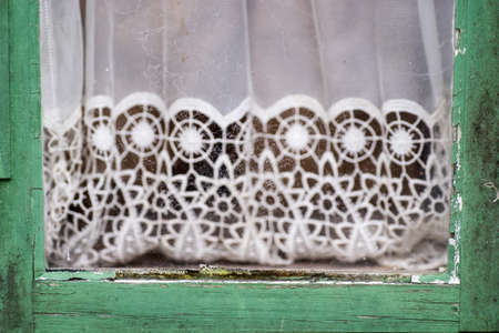 Green painted old cracked window with white lace curtains. Detail of vintage decorの写真素材