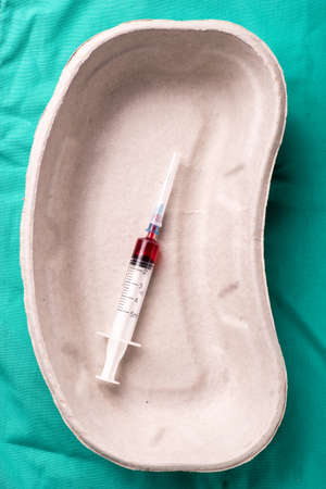Medical syringe with blood sample lying in a one use capsule on the hospital's green background. The background can be a textile part of a doctor or nurse's work uniformの写真素材