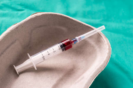 Medical syringe with blood sample lying in a one use capsule on the hospital's green background. The...