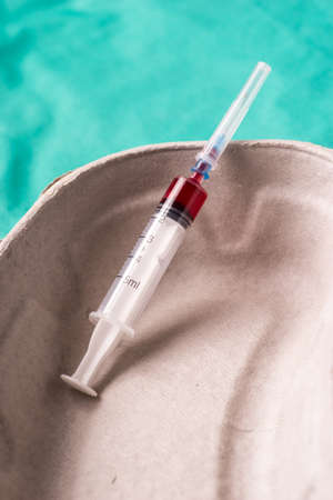 Medical syringe with bloodsample lying in a one use capsule on the hospital's green background. The background can be a textile part of a doctor or nurse's work uniformの写真素材