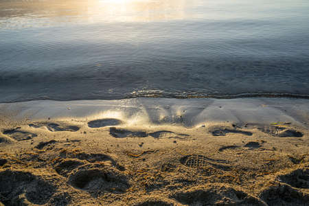 Beautiful sunrise at the clear calm sea, on the water's edge there are footsteps in the wet sandの写真素材